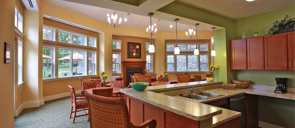 Community dining area with tables, chairs, fireplace, large windows, kitchenette, and overhead light fixtures