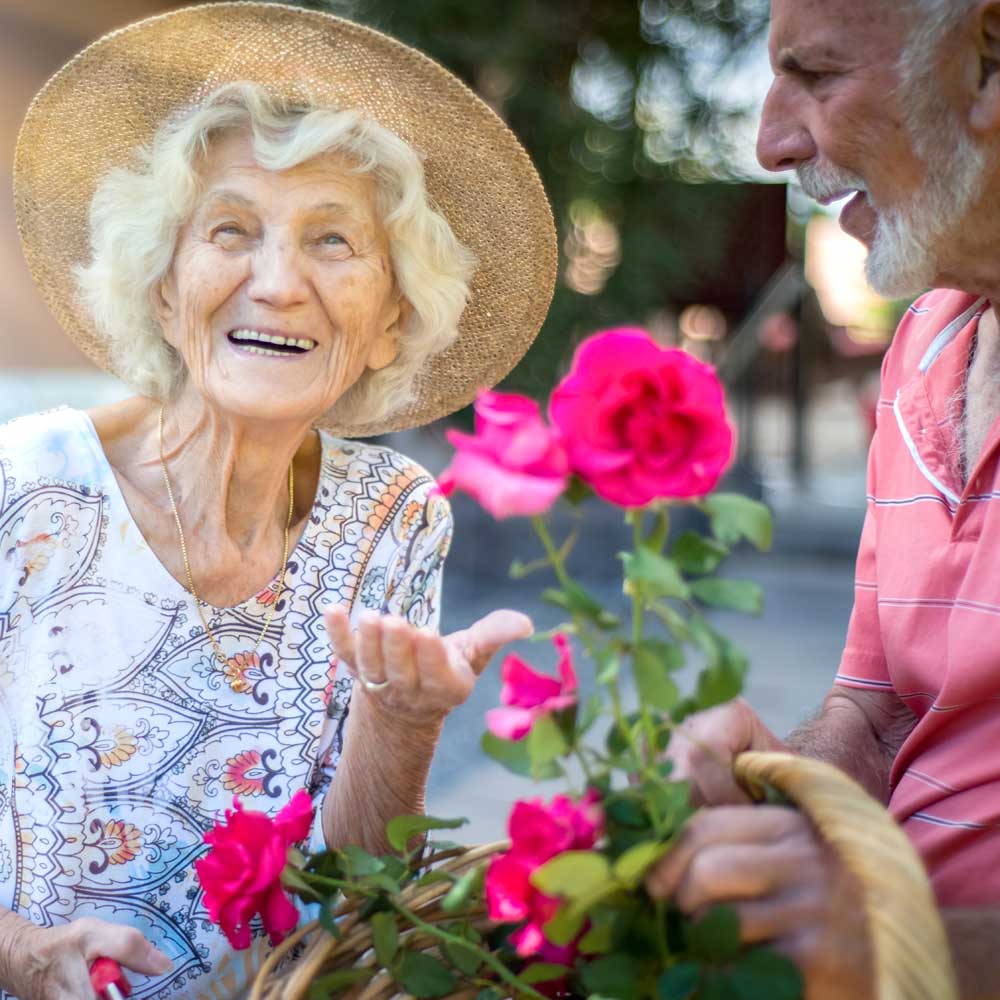 Male and female Marian resident smile and hold basket of pink flowers from garden`