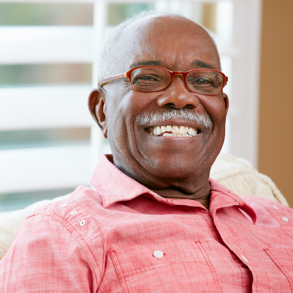 Older man with moustache wearing red-rimmed glasses smiles widely