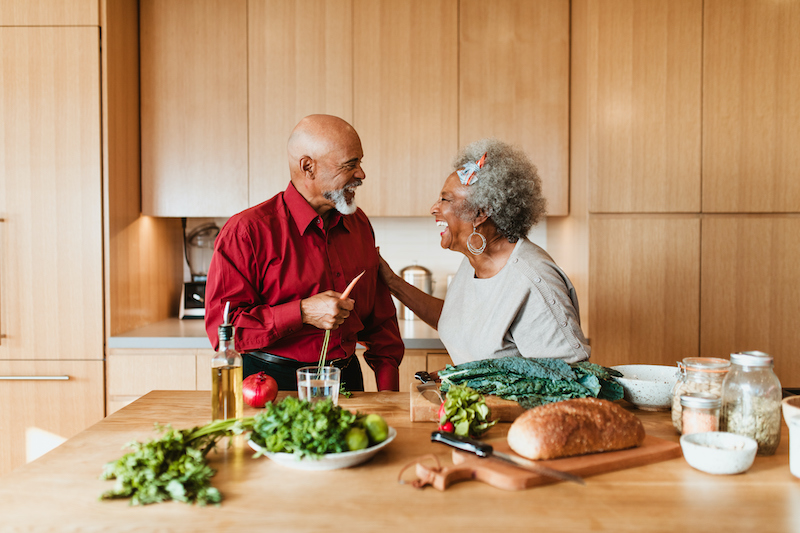 Cheerful older couple prepare vegan meal at kitchen island